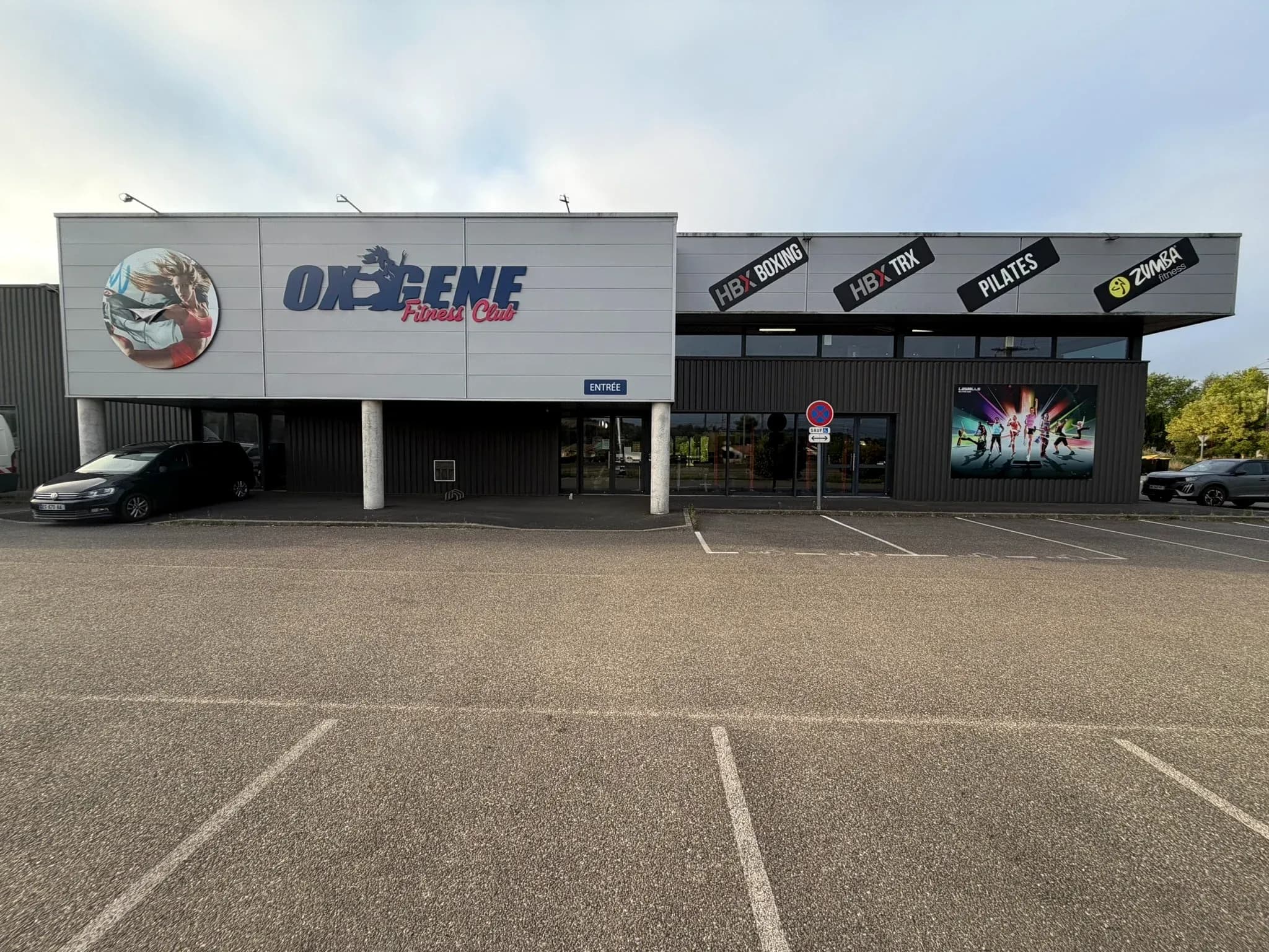 Vue frontale de la façade, de l’entrée et du parking d’OXYGÈNE Fitness Saint-Macaire.