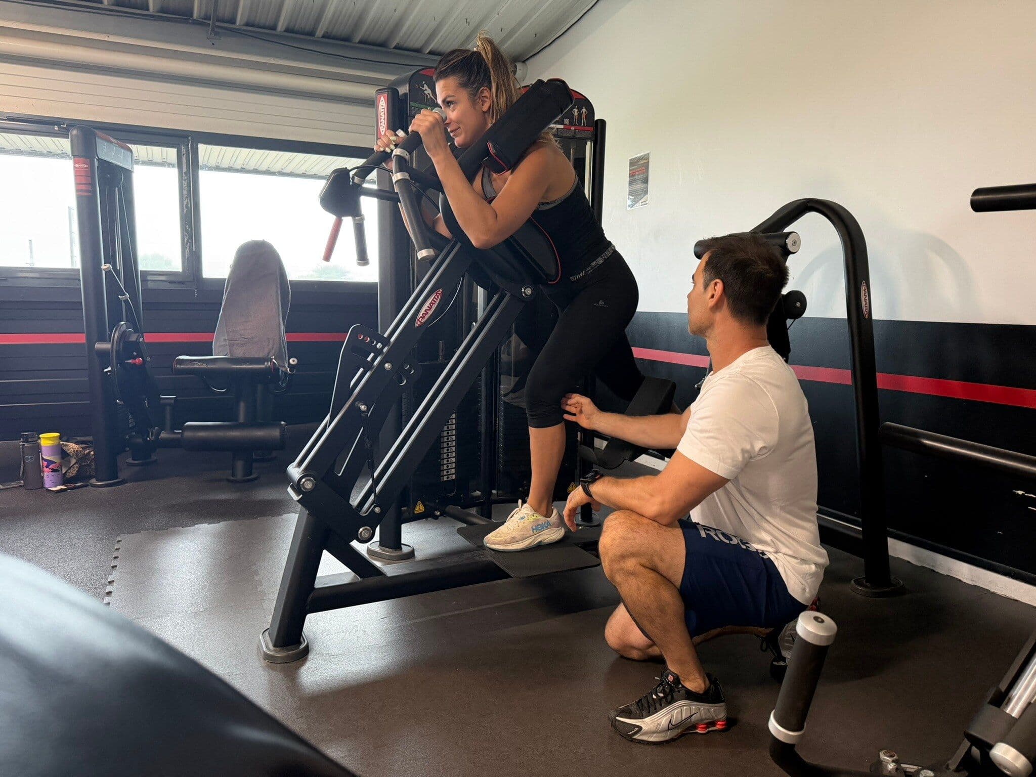 Un coach accompagne une adhérente pendant un exercice sur une machine de musculation.
