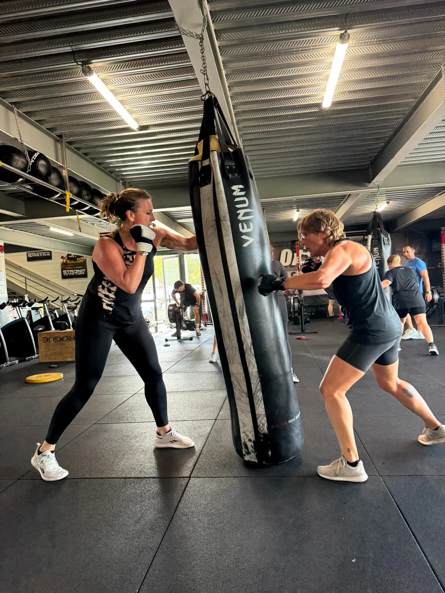 Deux participantes s’entraînent sur un sac de frappe pendant un cours FIGHT à OXYGÈNE Fitness Saint-Macaire.