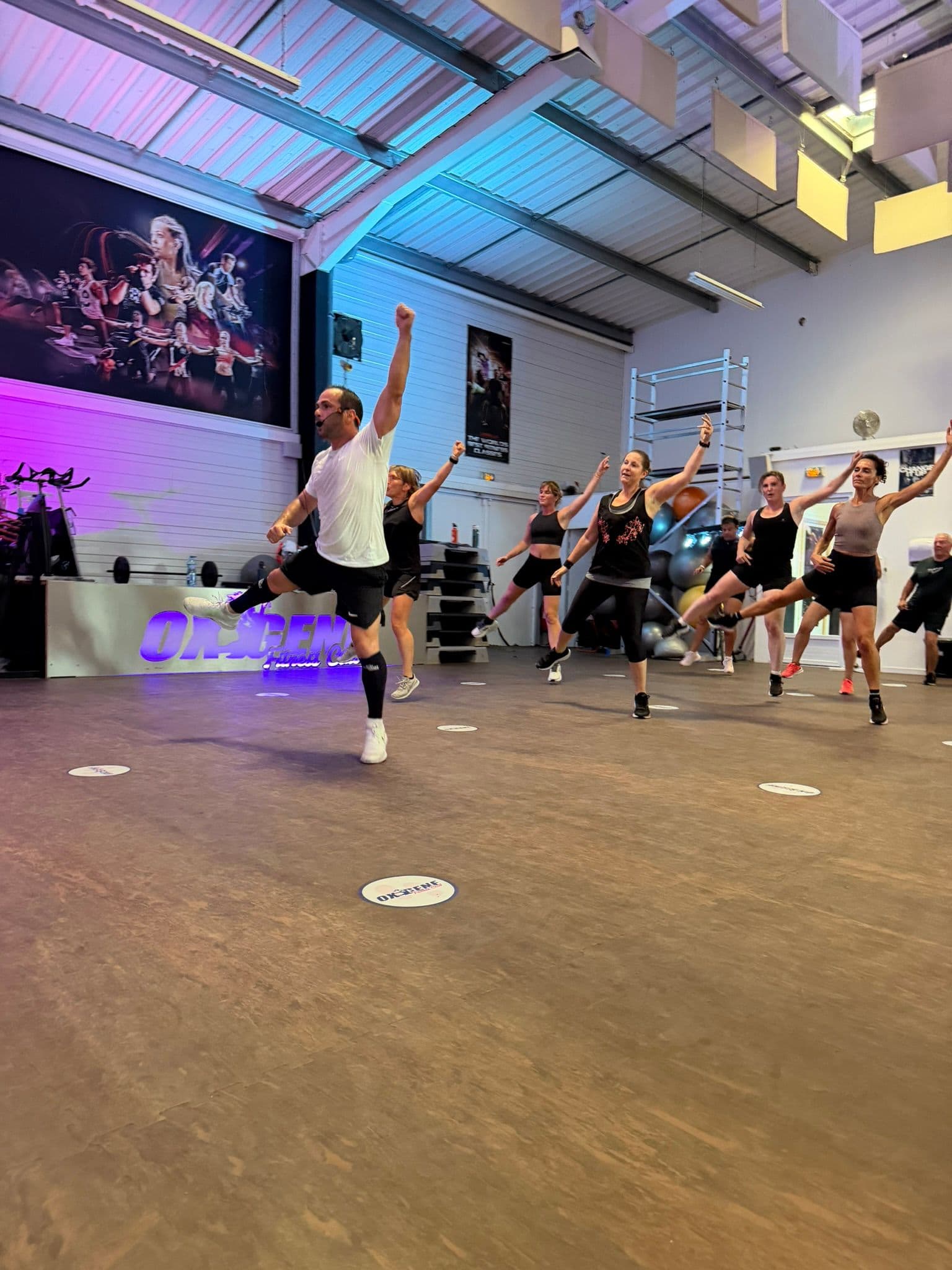 Coach et adhérents réalisant un mouvement dynamique coordonné pendant un cours collectif à OXYGÈNE Fitness Saint-Macaire.