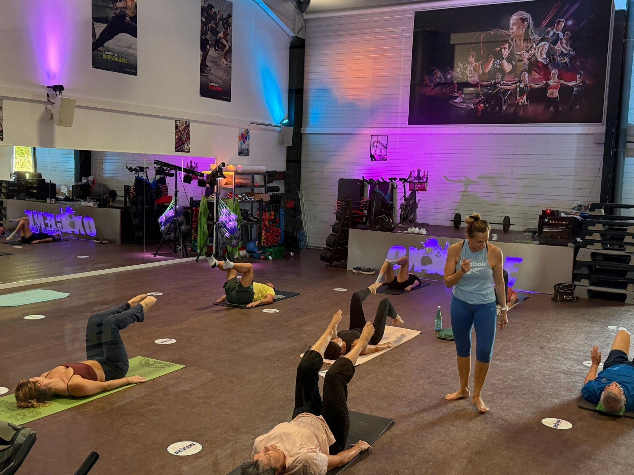 Un groupe d’adhérents réalise des exercices au sol pendant un cours collectif chez OXYGÈNE Fitness Saint-Macaire.