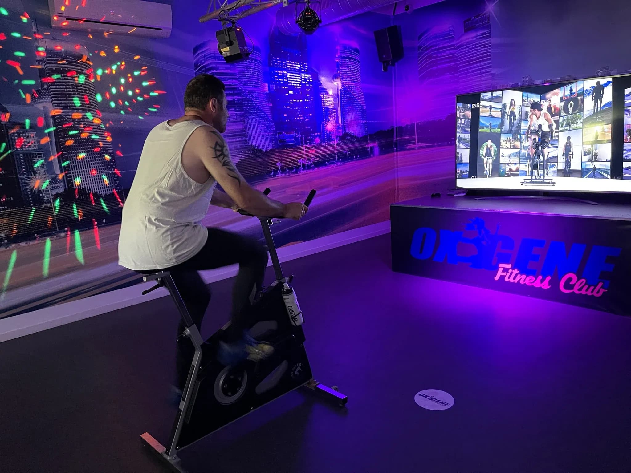 Adhérent sur un vélo face à un cours vidéo dans l’ambiance immersive de la salle virtuelle d’OXYGÈNE Fitness Saint-Macaire.